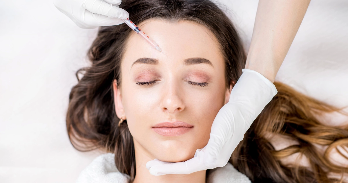 A person with their eyes closed is receiving a Botox injection on their forehead from a gloved hand holding a syringe for Botox in Fountain Valley, CA.